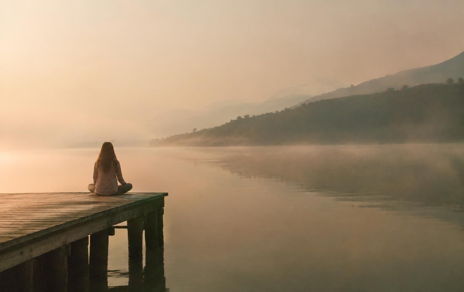 Mulher meditando à beira de um lago ao amanhecer